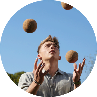 Person jongliert mit braunen Bällen vor blauem Himmel